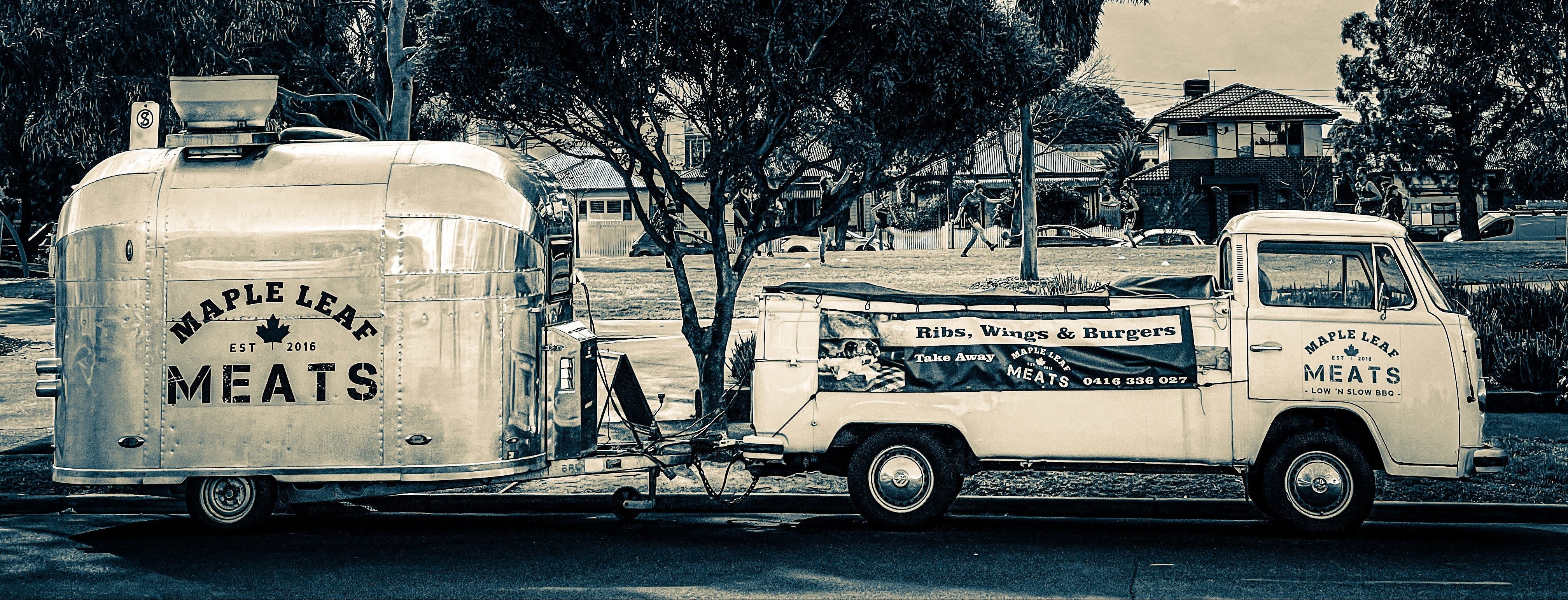 Vintage truck and trailer with 'Maple Leaf Meats' branding parked under trees.
